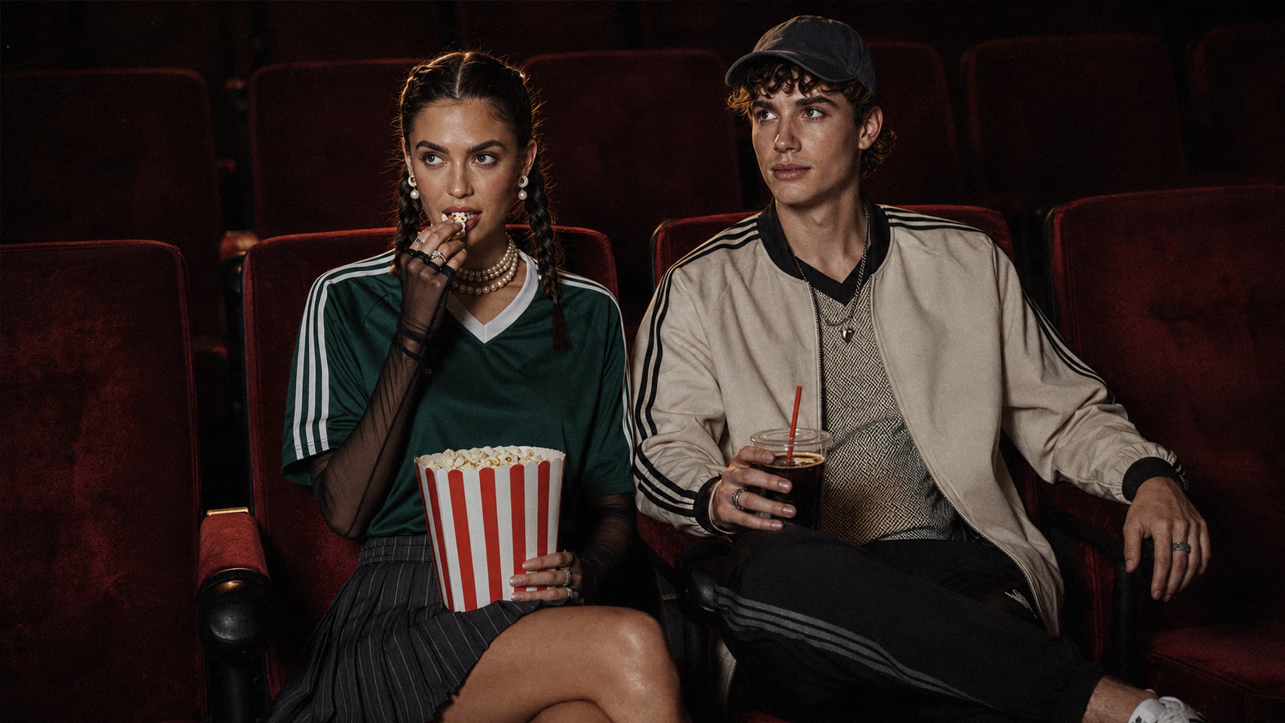 Visual lifestyle generato con AI: due giovani in look sportivo seduti nelle poltrone rosse di un cinema, con popcorn e bibita.