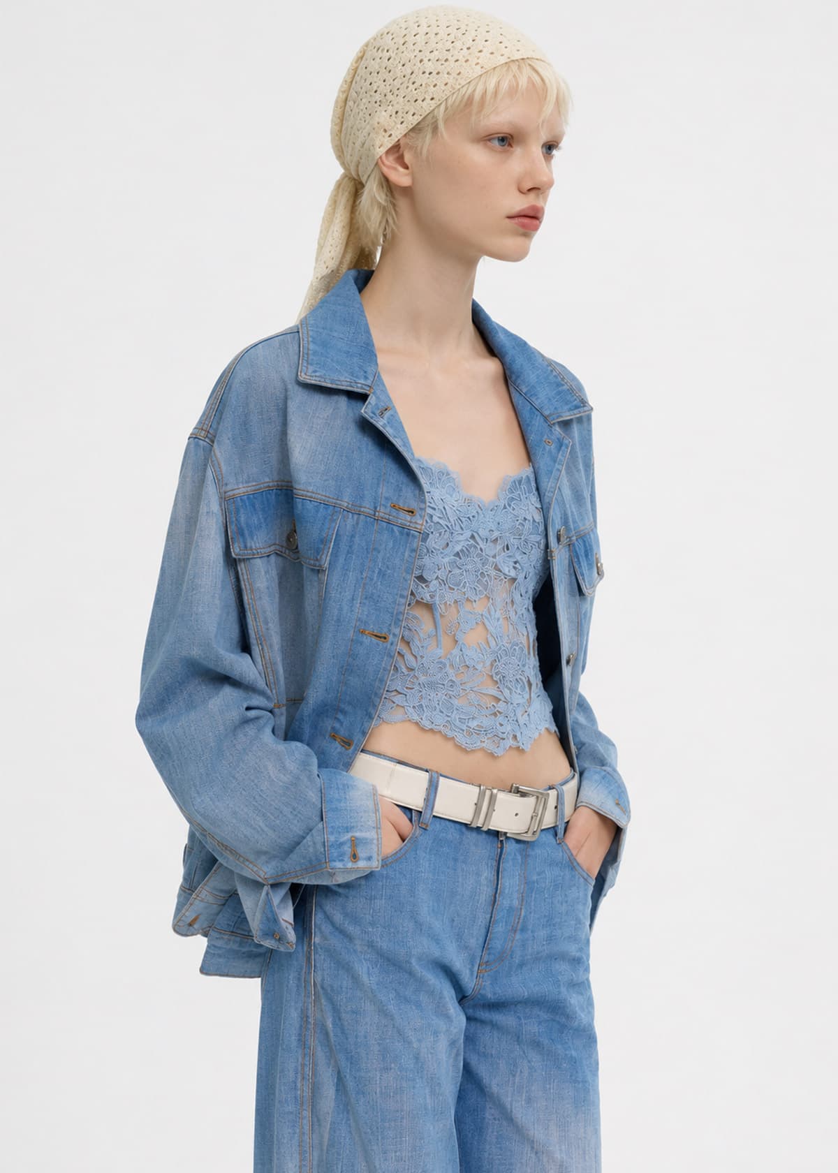 Capo indossato da un talento AI: giacca di jeans su top in pizzo azzurro, con cintura bianca, su fondo bianco.