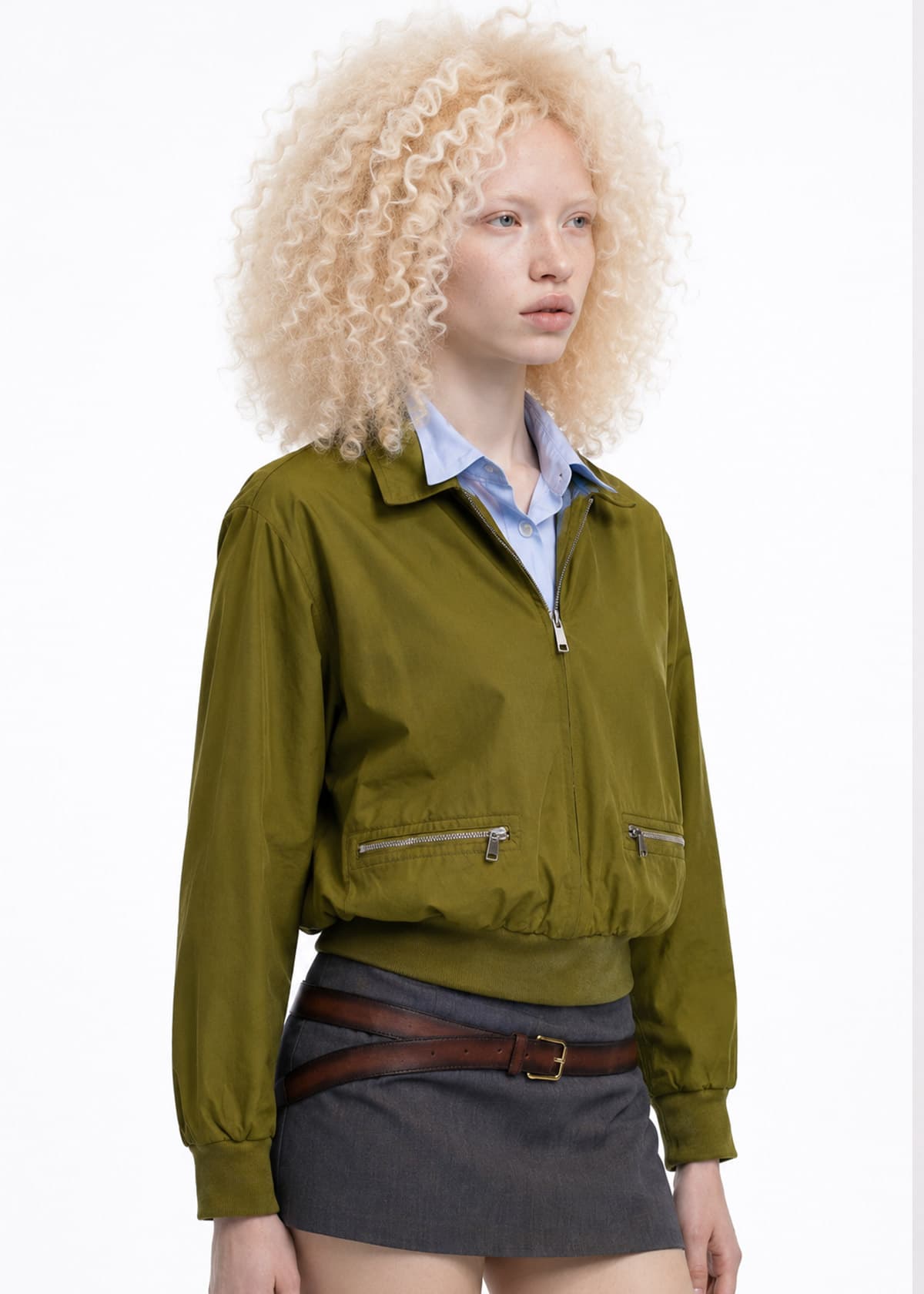 Capo indossato da un talento AI: blouson verde oliva con tasche a zip, portato su camicia azzurra.