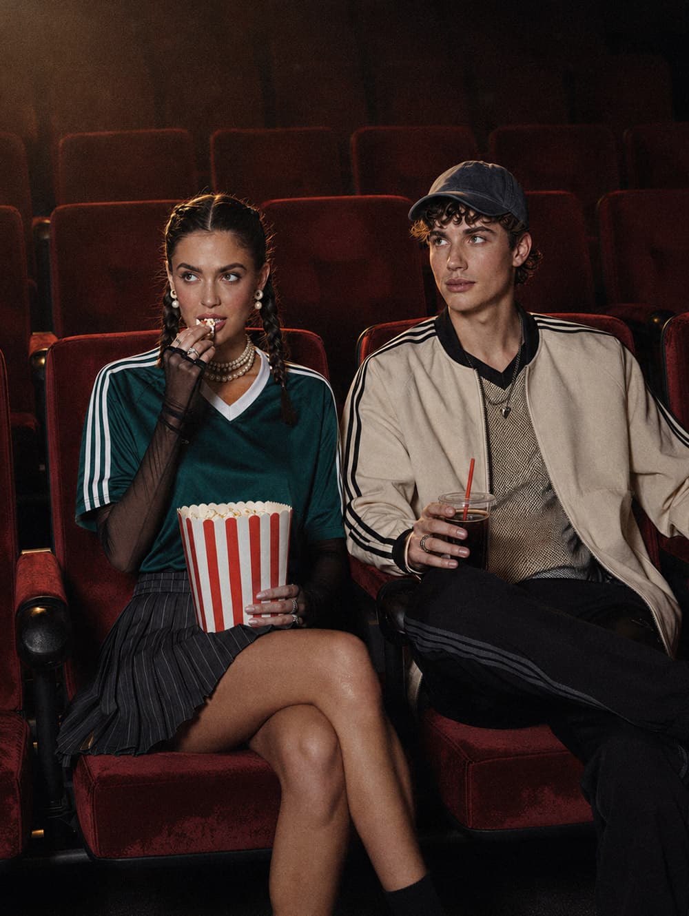 Visual lifestyle generato con AI: coppia in look sportivo nelle poltrone rosse di un cinema, con popcorn e bibita.